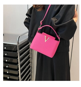 Magenta lychee leather handbag with V-shaped gold buckle shown as a crossbody bag