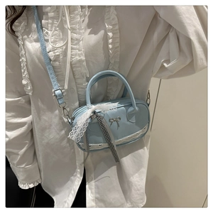 Detail of light blue crossbody bag with bow emblem, lace trim and plaid ribbons