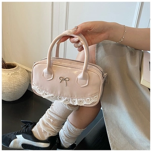 Close-up of pink patent leather Boston bag with white lace trim and bow buckle detail
