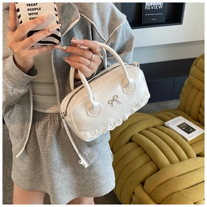 Detail of white Boston bag with silver bow accent and delicate lace trim on the bottom