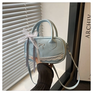 Light blue matte leather handbag with metal bow and heart lace detail on table