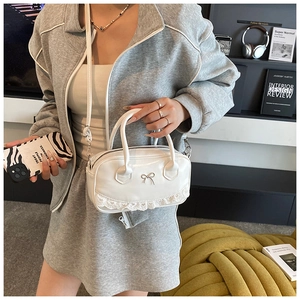 Detailed view of white ballet style handbag with lace trim and metallic bow accent
