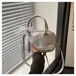 Detail of silver metallic handbag featuring bow charm and lace trim with soft light