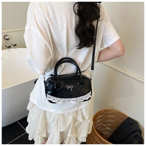 Detail of black Boston bag featuring golden bow and white heart lace trim detailing