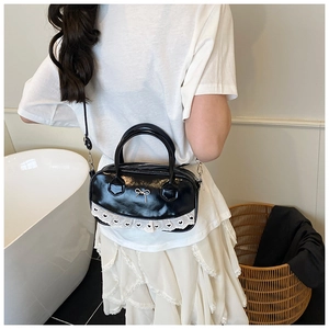 Detail of black patent leather crossbody bag with lace trim and gold bow accent