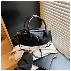 Detail of black glossy Boston bag with silver metal bow and delicate white lace trim
