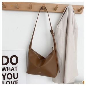 Detailed view of brown leather tote bag hanging with stylish wide strap and golden logo
