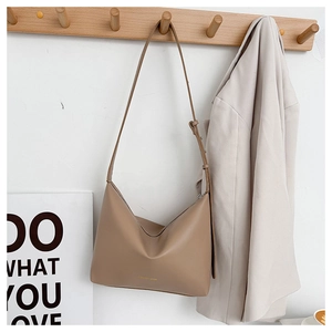Minimalist khaki leather tote bag hanging on wooden hook in lifestyle setting