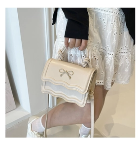 Close-up of cream square shoulder bag with wavy edge and golden bow metal buckle