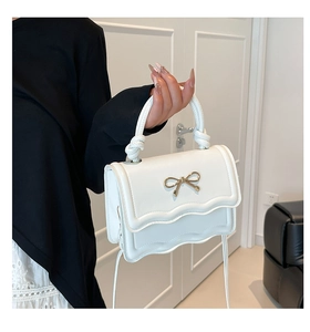Close-up of white structured handbag with golden bow metal charm and scalloped edge detail