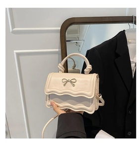 Detail of cream crossbody bag with metal bow accent and wavy edge flap design