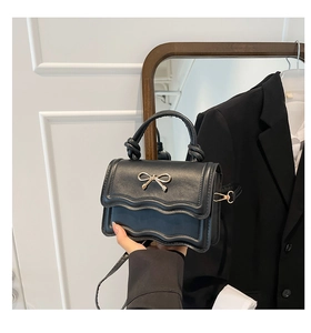 Detail of black mini crossbody bag featuring scalloped edges and gold bow decoration