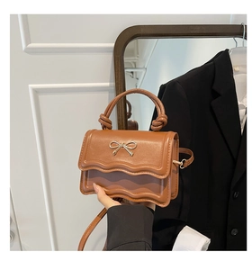 Close-up of brown mini handbag featuring wavy edge flap and golden metal bow detail