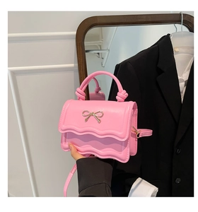 Detail of pink bow handbag with scalloped flap and golden metal bow decoration
