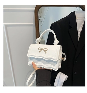 Detail of white mini bag with golden bow hardware and wavy edge flap design