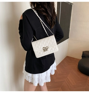 Sac bandoulière beige matelassé avec nœud métallique porté par un mannequin avec élégance
