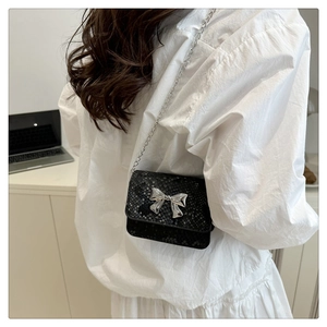 Detail of black snake-textured mini crossbody bag with a silver metal bow accent
