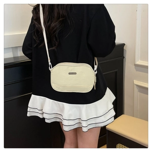 Detailed back view of a minimalist cream nylon crossbody bag on model for scale