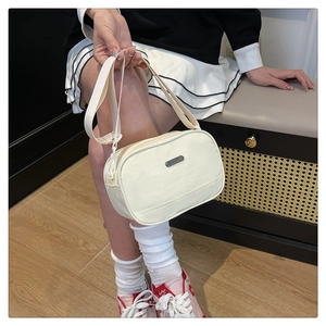 Detail of adjustable strap and silver logo plate on beige nylon crossbody bag
