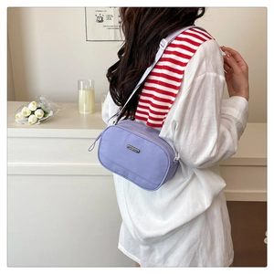 Detail of purple nylon crossbody bag with metal logo and adjustable white strap on model
