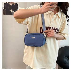 Blue nylon crossbody bag with adjustable strap and metal logo plate on model