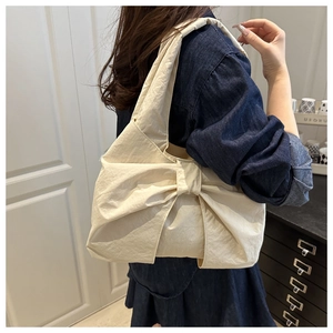 Détail d'un sac cabas beige avec un grand nœud et une texture en nylon plissé