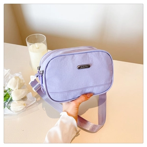 Close-up of light purple nylon crossbody bag with metal logo and adjustable strap