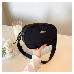 Detail of black nylon crossbody bag with silver metal logo plaque and zipper