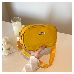 Detail view of bright yellow nylon crossbody bag with multi-layer zippers and silver logo