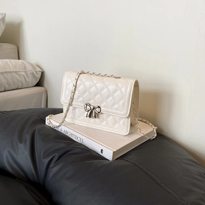 Sac bandoulière matelassé blanc cassé élégant avec nœud argenté sur fond de livre d'art