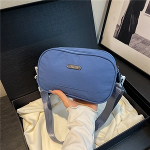 Blue nylon crossbody bag with adjustable grey strap and metal logo on white satin in box