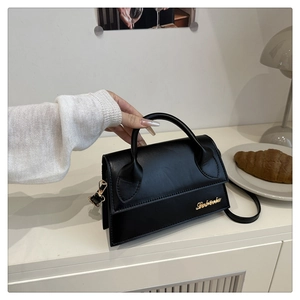 Gros plan sur un sac bandoulière noir minimaliste avec logo doré sur table