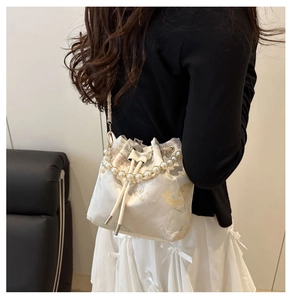 Detail of cream drawstring bucket bag with gold floral fabric and pearl handle