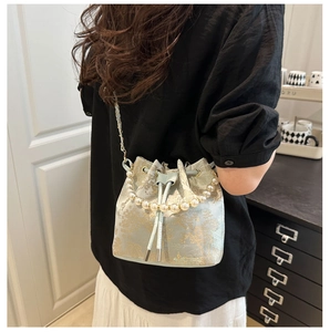 Detail of light blue bucket bag with floral embroidery and pearl handle worn by model