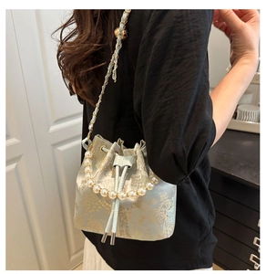 Detail of light blue bucket bag featuring mountain embroidery and pearl handle strap