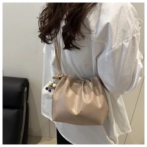Detail of apricot pleated bucket bag with plush charm on a model in white shirt