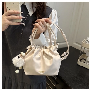 Detailed macro view of cream drawstring bucket bag featuring a white plush crown charm