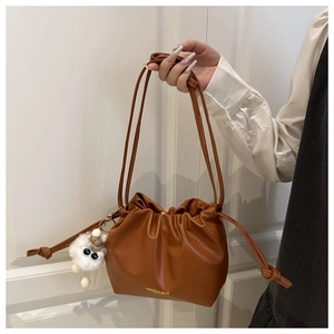 Brown leather drawstring bucket bag with gold lettering and white plush monster charm