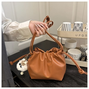 Close-up of brown pleated bucket bag with gold lettering and white plush charm