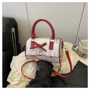 Detail of red and white Boston bag featuring lace trim, bow, and heart pendant