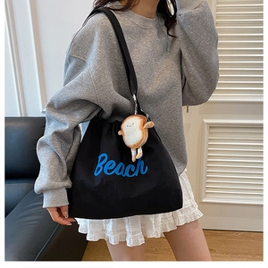 Close-up of black canvas tote bag with blue Beach embroidery and cute toast plush charm