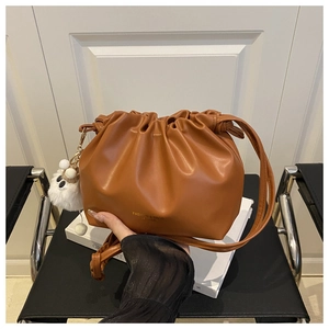 Detail of brown leather drawstring bucket bag with fashion logo and fluffy pompom charm