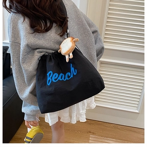 Detail of black canvas tote bag with blue Beach lettering and plush toast charm
