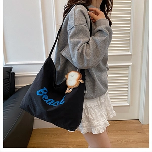 Detail of black canvas tote bag with Beach embroidery and toast plush charm accessory