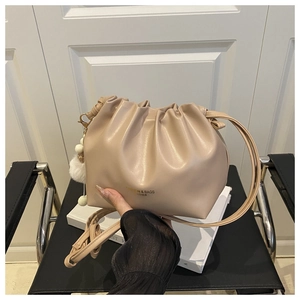 Detail of beige pleated drawstring bucket bag with gold lettering and plush charm