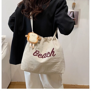 Beige canvas tote bag with red Beach text and cute bread plush charm on model