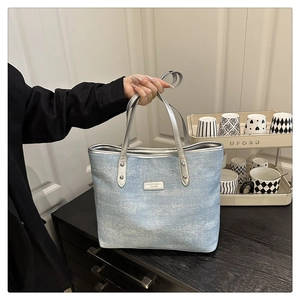 Detail of light blue tote bag with silver handles and metal label held in hand