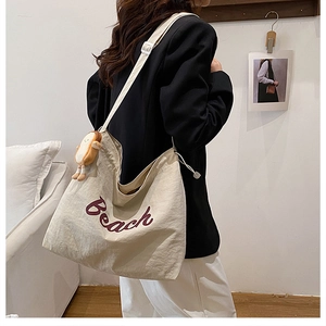 Detail of off-white canvas tote bag featuring Beach embroidery and cute toast plush charm