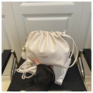 Detail of cream pleated bucket bag with plush ball charm and drawstring closure