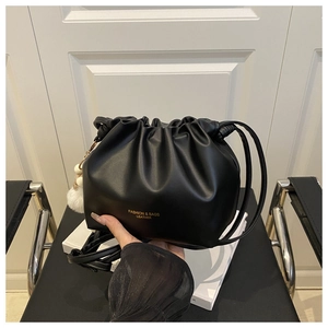 Detail of black pleated cloud bucket bag with gold logo branding and white pompom charm